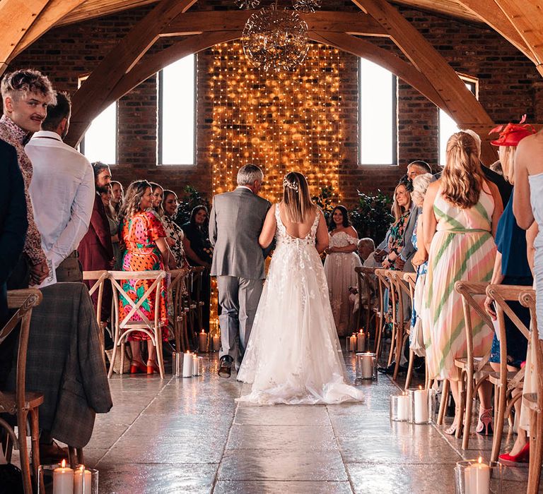 Bride in lace wedding dress walking down a candlelit aisle for the same sex wedding 