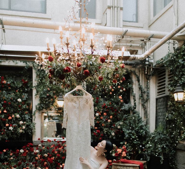 The bride's long sleeve Pronovias wedding dress hanging in the centre of the aisle surrounded by the red wedding flowers 