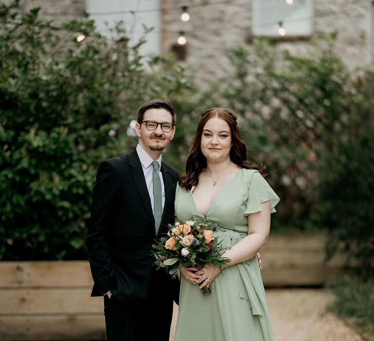 Bridesmaid in green dress is with her partner on the wedding day with a wildflower wedding theme 