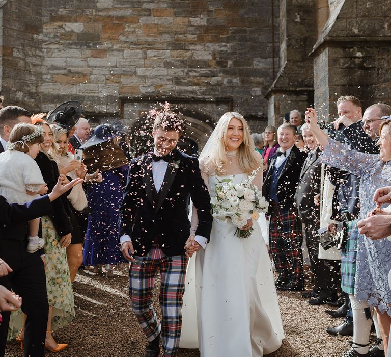 The bride and groom walk out to confetti after their wedding 