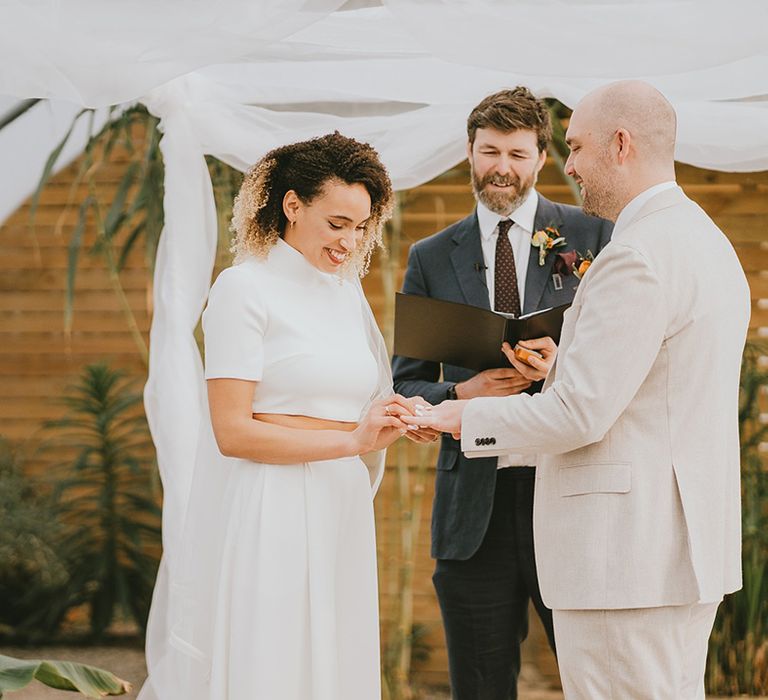 Groom in cream suit place the bride's ring on her finger for the wedding 