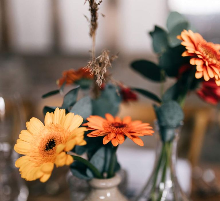 Yellow and orange poppies and eucalyptus in small ceramic vases as wedding tablescape centrepieces on wooden slates 