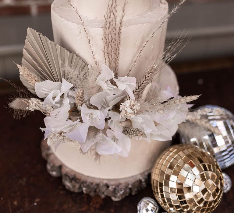 white iced wedding cake with white dried wedding flowers and disco balls 