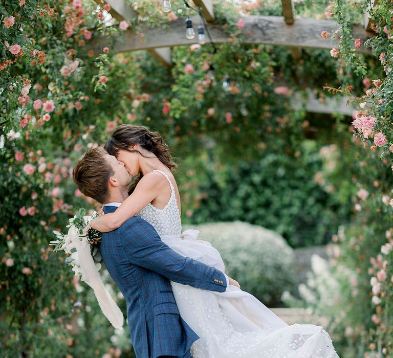 groom in a navy suit kissing his bride in a Made With Love bridal gown in the gardens at Euridge Manor 