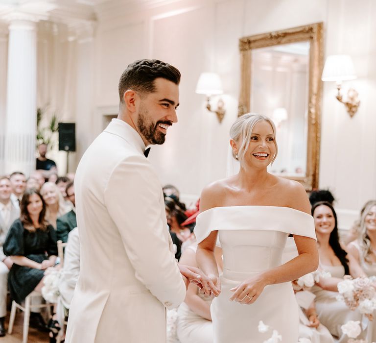 Bride in modern classic off the shoulder Eva Lendel wedding dress with groom in white double breasted suit 