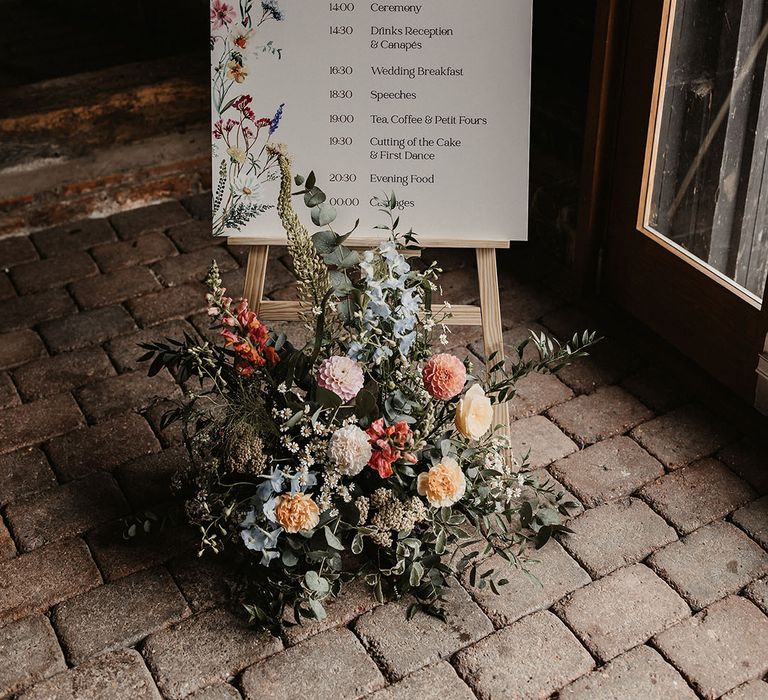 Wedding order of service and welcome sign covered in colourful painted wedding flowers 