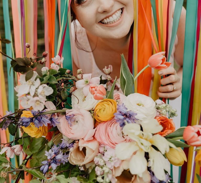 Bride peeping through colourful ribbon streamer decorations at boho festival wedding 