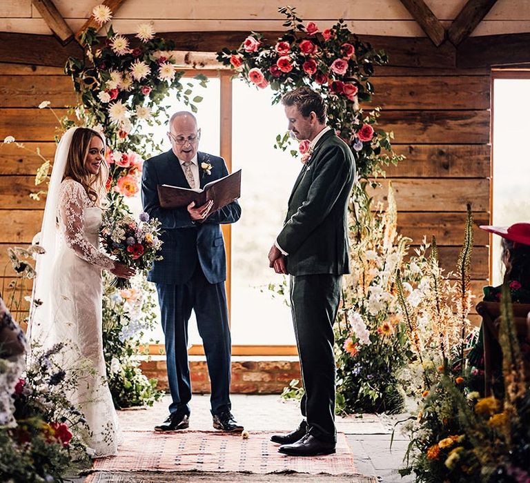 Wedding celebrant stands in between flower columns with the bride and groom 