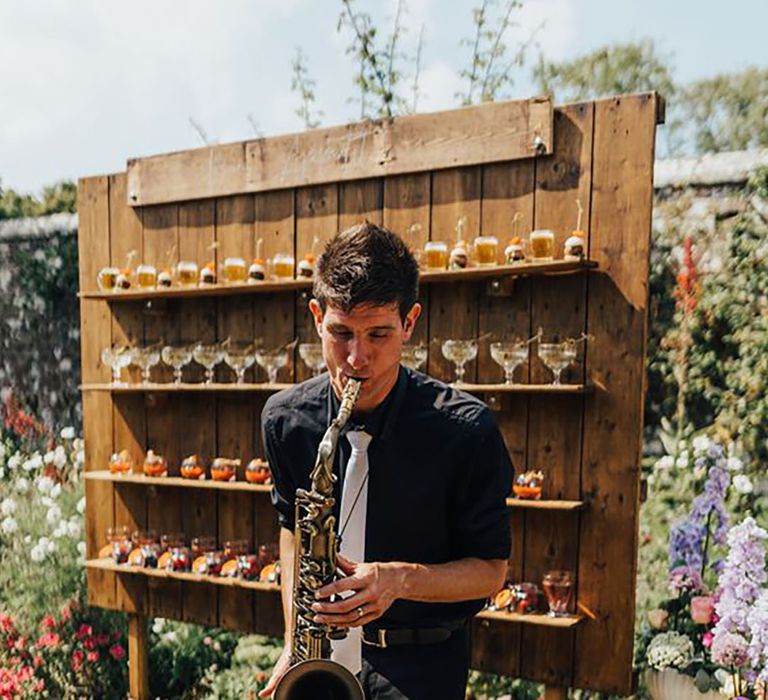 Drinks cocktail wall for wedding guests sitting behind a live saxophone player