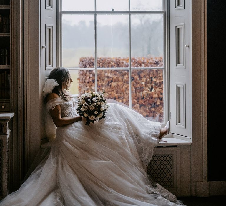 Bride in princess wedding dress gazing out of the window at the luxe country house in Dorset 