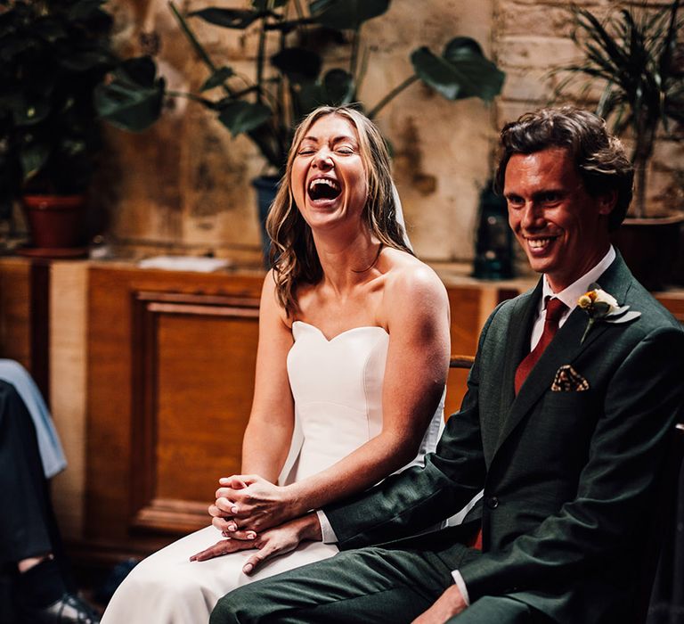 Bride in strapless wedding dress sitting with groom in green suit during their ceremony 