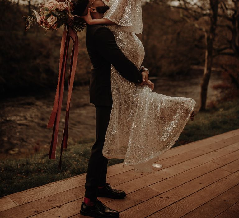 Groom picking up his bride in a sparkling wedding dress