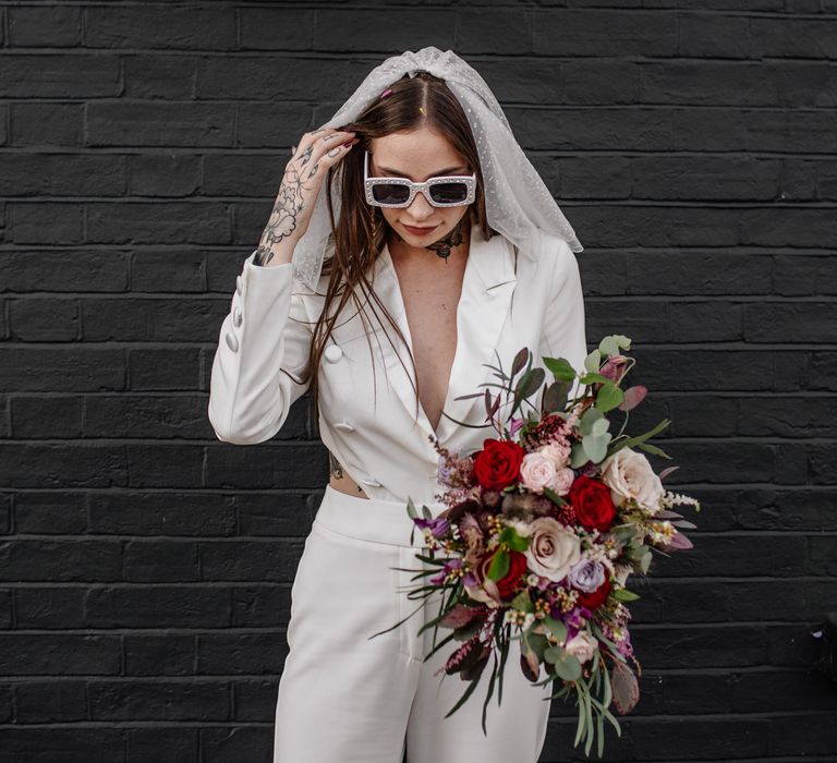 Stylish bride in a jumpsuit, sunglasses and polka dot veil 