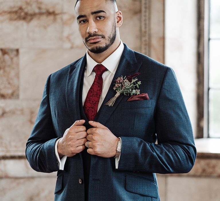 Stylish groom in navy suit with maroon tie 