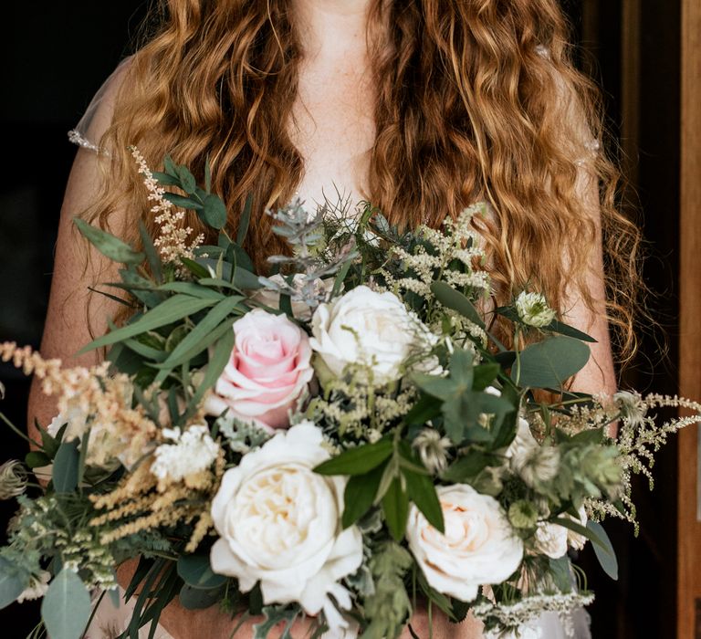 Bride wearing appliqué wedding dress holding floral bouquet with pink roses