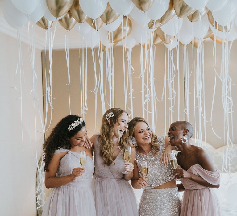 Bride in sparkly wedding dress laughing with her bridesmaids on the wedding morning in chiffon dresses 