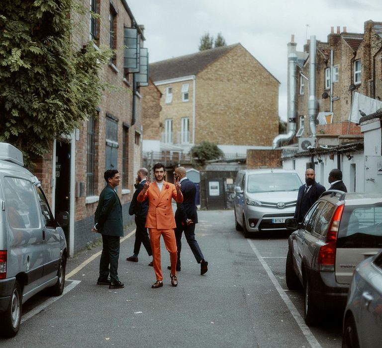 Stylish groom in a double breasted orange suit standing in the street 