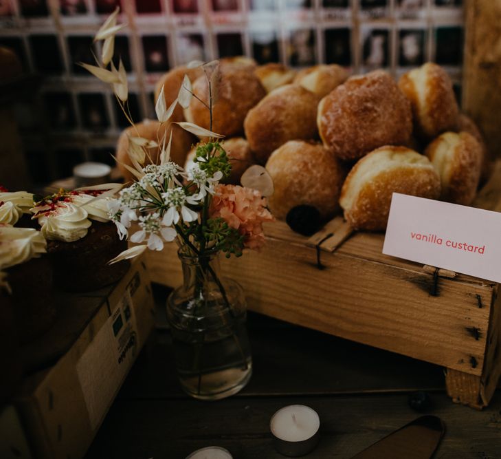 Bud vase of wildflowers in front of a crate of vanilla custard doughnuts