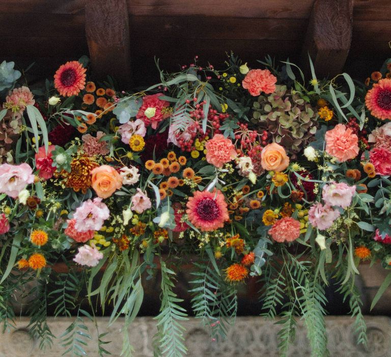 A large centrepiece flower display of orange, red and pink blooms, including carnations, roses and daisies