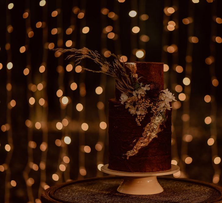 Two-tier wedding cake with dried flower decor in front of a fairy light canopy 