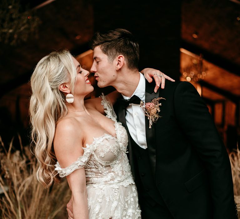 Groom in a black tuxedo leaning his bride down for a kiss at their neural wedding theme celebration