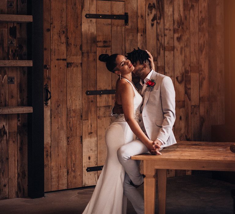 Groom sits on table as bride embraces him 