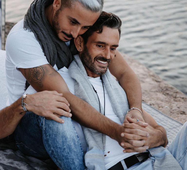 Groom leans back into boyfriend and they wrap their arms around one another