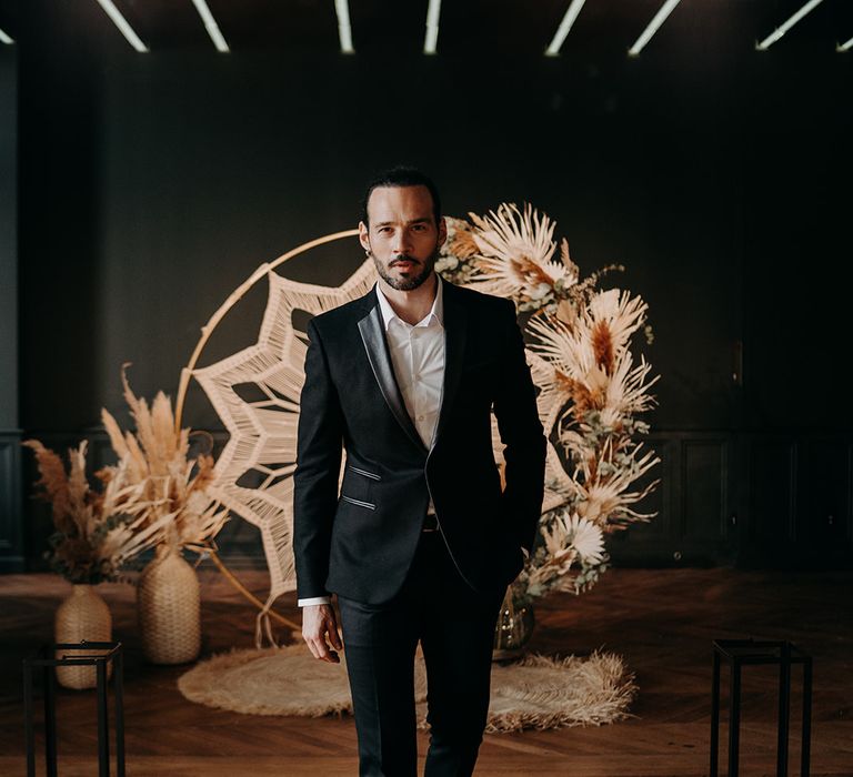 Groom walks away from macrame backdrop whilst wearing black tailored suit