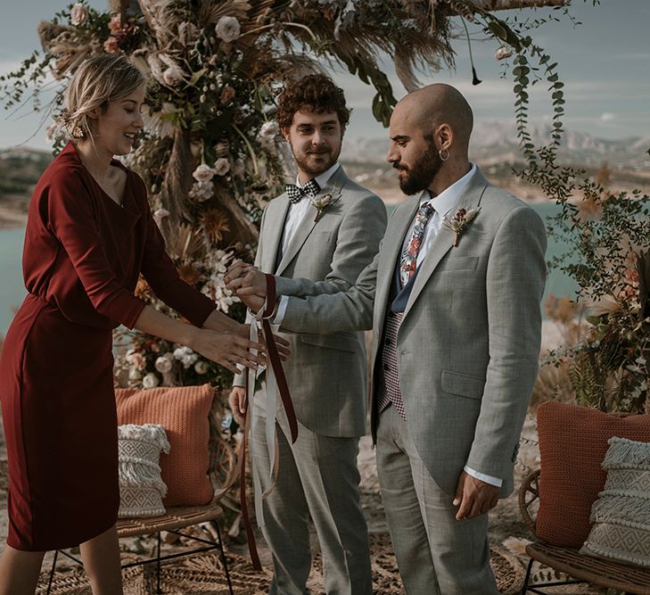 A celebrant fastens a gay couples hands as part of their wedding ceremony. Photography by Mas Positivo Producciones.