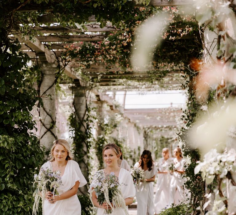 Bridesmaids walk through pergola on wedding day 