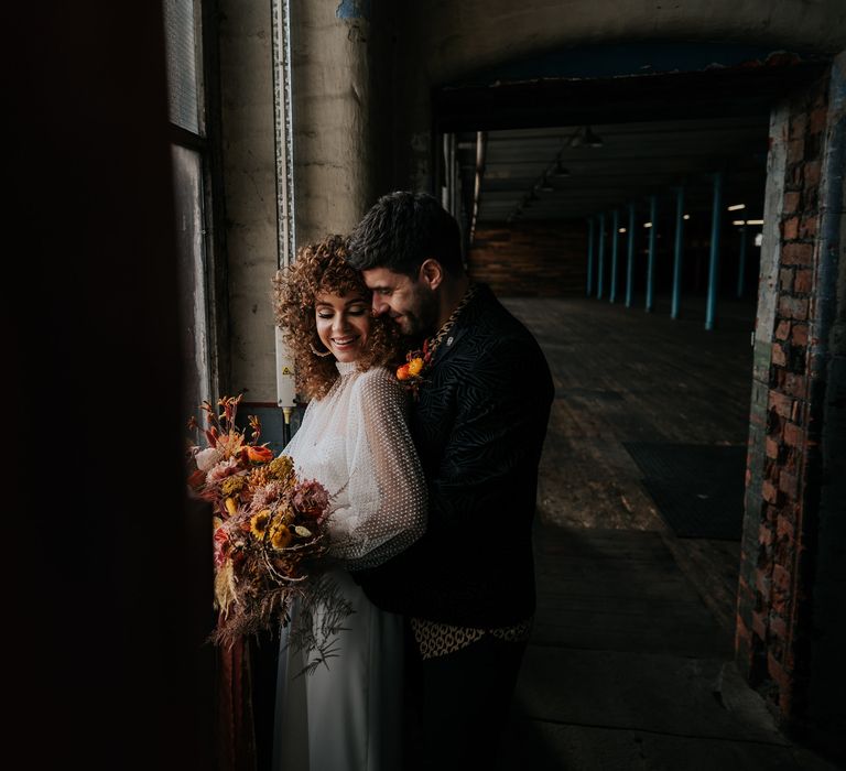 Groom embracing his bride at their 70s industrial wedding with the bride wearing a jumpsuit 