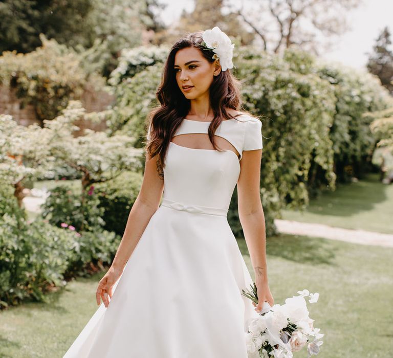 Bride in a Suzanne Neville princess wedding dress with tiny bow waist detail and cape with orchid flowers in hair 