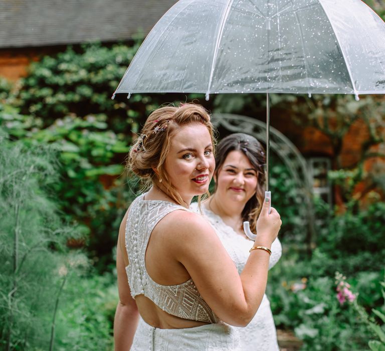 Lesbian brides stand under umbrella together on their wedding day for Park Farm wedding