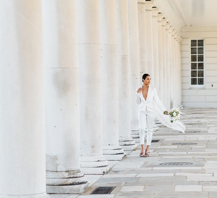 A bride at a black a white wedding wears a bespoke low cut white suit, a long veil and carries black and white wedding flowers.