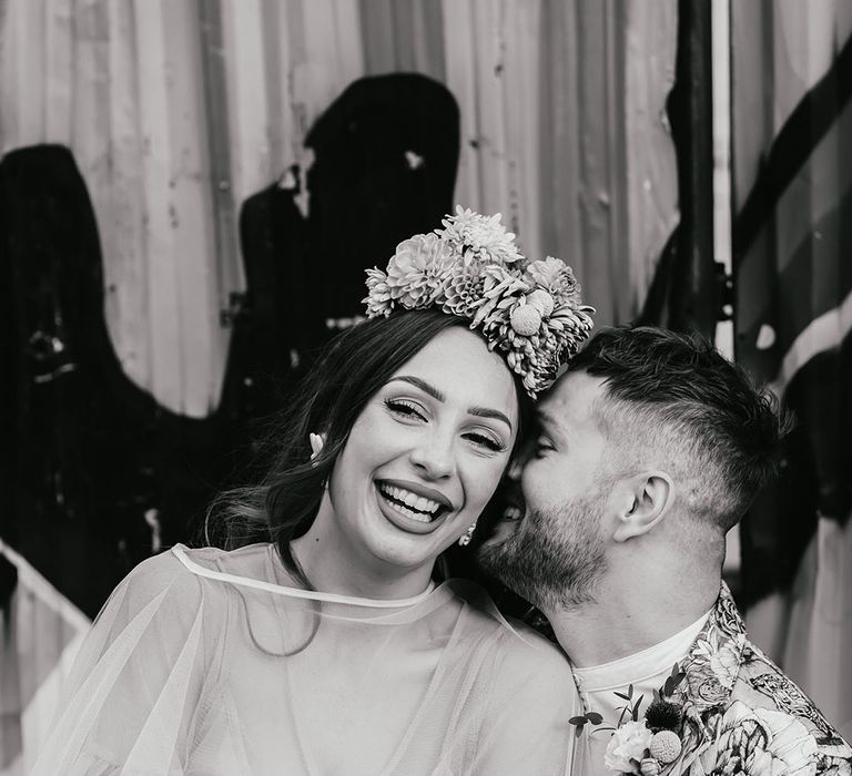 Black and white portrait of a disabled groom in a patterned jacket laughing with his bride in a flower crown 