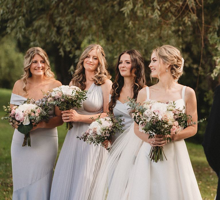 Bride in a Stella York wedding dress looking back at her bridesmaids during the wedding ceremony in light grey dresses with pink and white bouquets