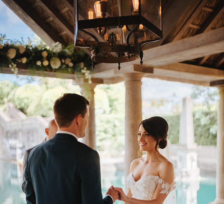 Bride & groom look lovingly at one another as they hold hands during ceremony on their wedding day