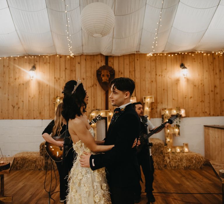 Bride in strapless feathered wedding dress and headpiece hugs groom in dark blue suit during Wellbeing farm wedding ceremony in Lancashire