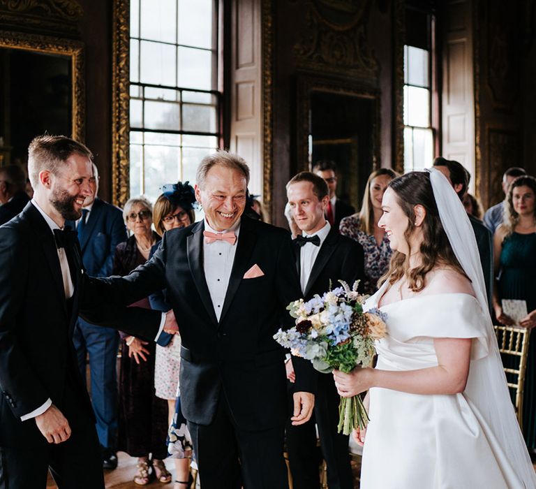 Bride & groom stand in front of one another during ceremony as bride holds pastel bouquet