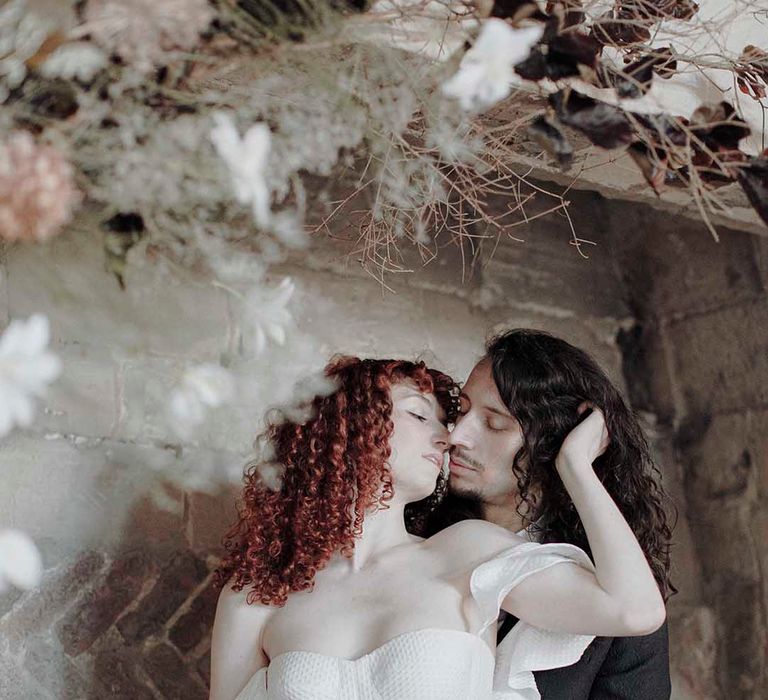 Groom with long hair kissing his bride with red naturally curly hair in a strapless wedding dress at Blackfriars Priory 