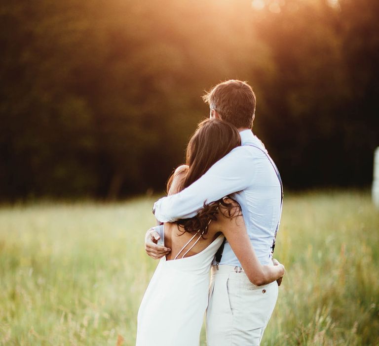 Bride & groom embrace outdoors as they watch the sun set