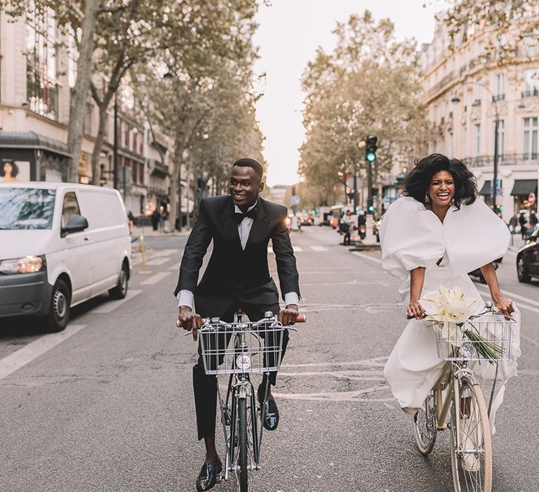 South Asian bride and Black groom in a princess wedding dress and black tuxedo riding bicycles through Paris wedding elopement 