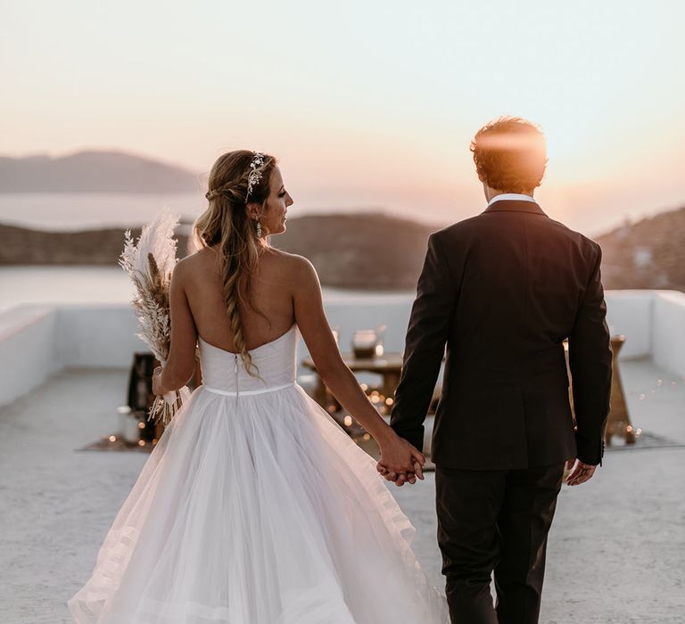 Bride & groom hold hands as they walk together as the sun begins to set 