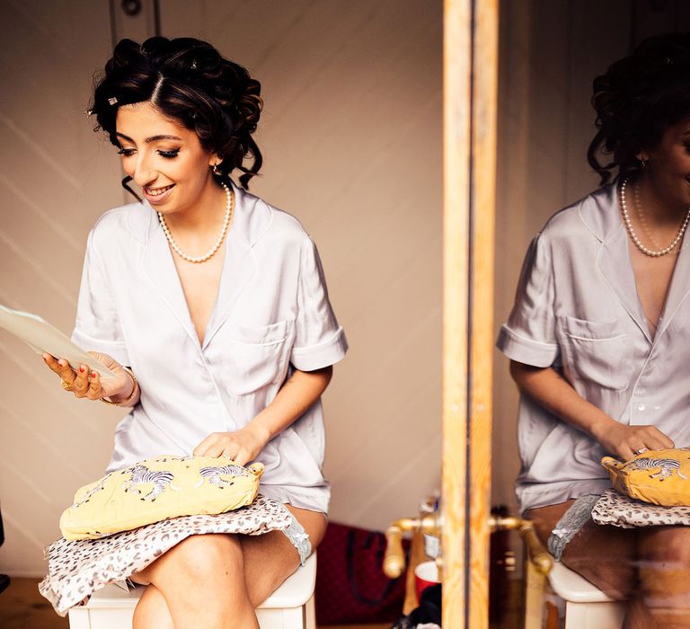 Bride in short sleeve bridal pyjamas and pearl necklace sits reading letter before wedding