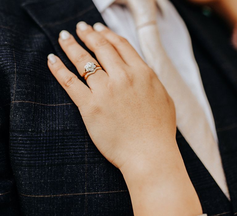 Bride wears flower shaped diamond wedding ring as she places hand on grooms check suit