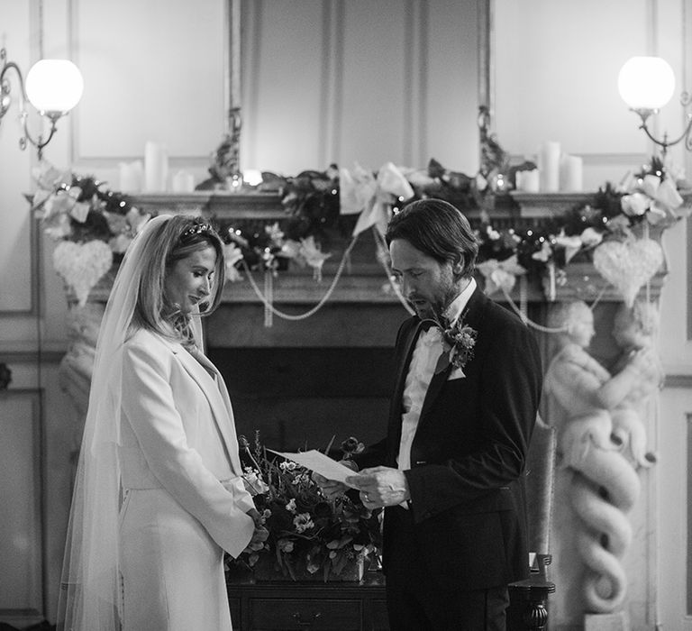 Bride & groom stand in front of fireplace complete with wreath on their wedding day