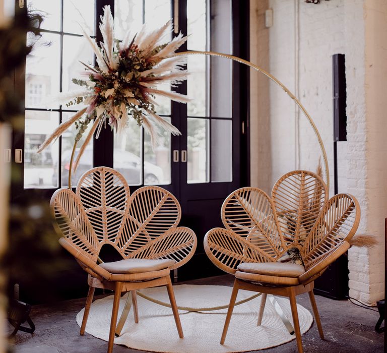 Private seating area for the bride and groom with a wooden moongate with dried flower decor and two wooden flower rattan chairs 