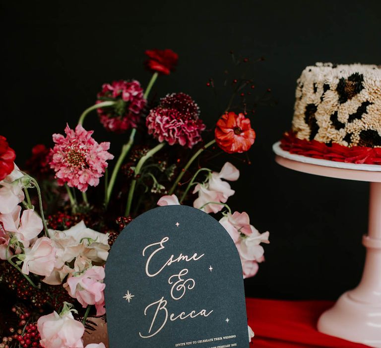 Leopard print buttercream wedding cake and black wedding invitation ith gold foil lettering and red tassel 