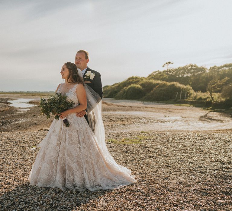 Bride and groom stand together on the private beach at country house wedding venue 