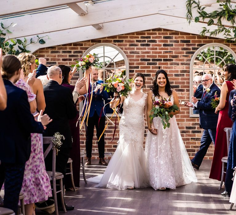 Bride in lace mermaid style tulle wedding dress with bride in floral lace wedding dress walk back down the aisle together 